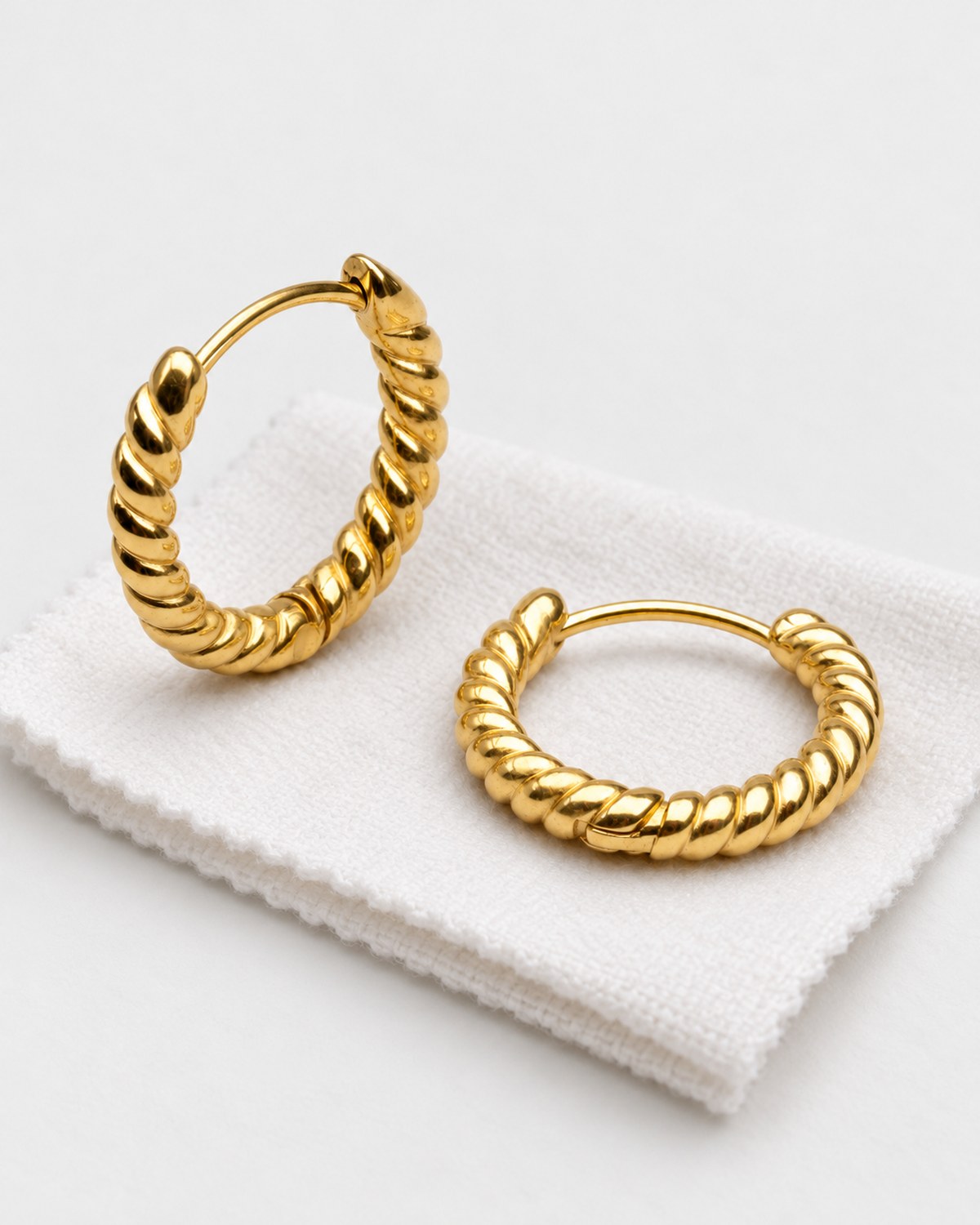 Gold-tone twisted hoop earrings resting on a soft jewellery-care cloth