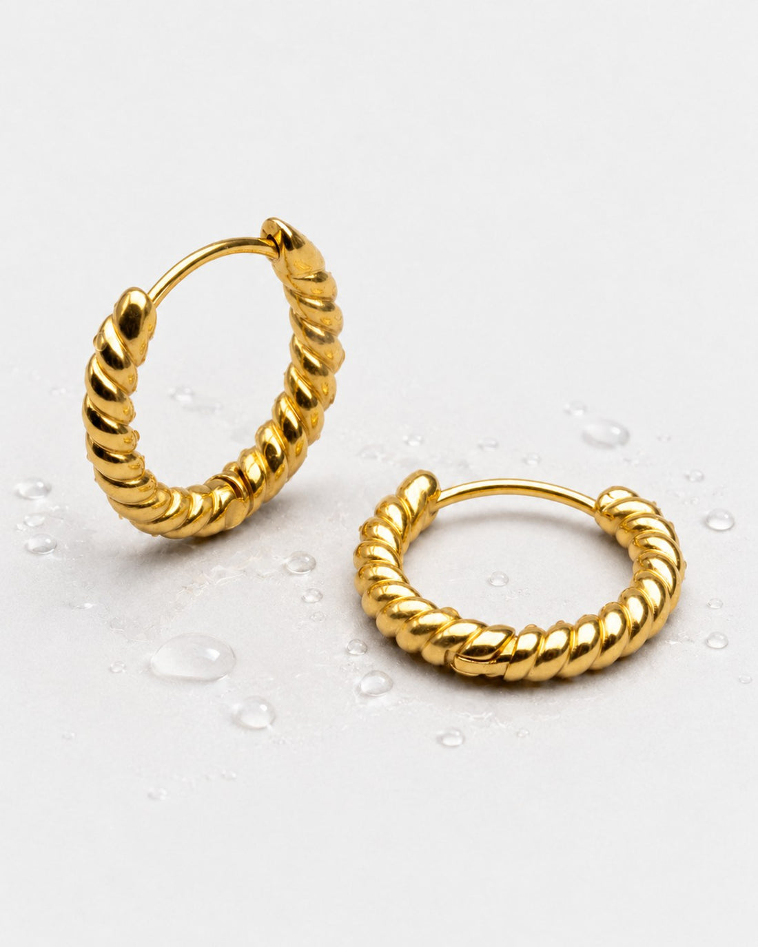 Gold-tone twisted hoop earrings beside water droplets