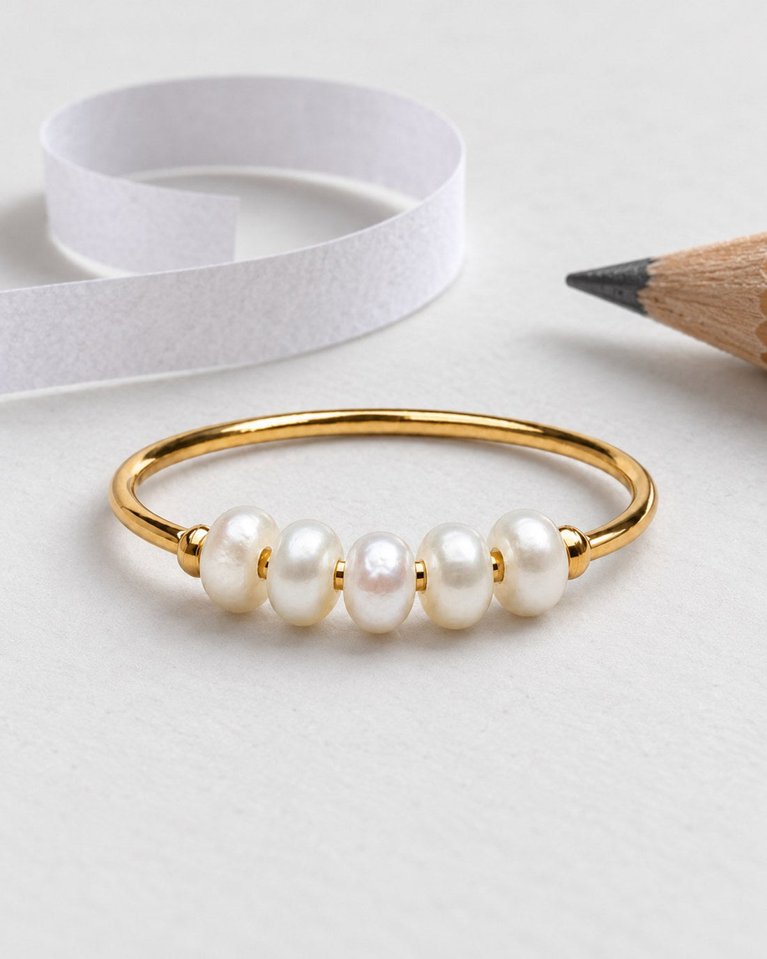 Gold-tone ring with five smooth white oval accents beside a paper strip and pencil