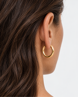 Gold-tone rounded hoop earring worn beside the jaw and neck